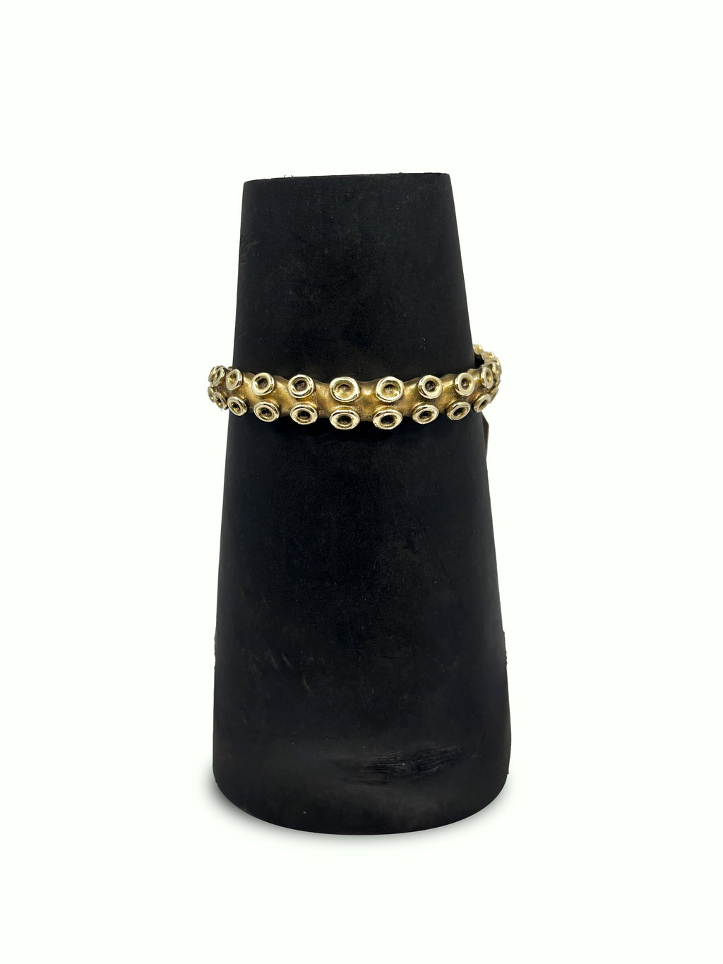 Gold bracelet on a black velvet stand against a white background