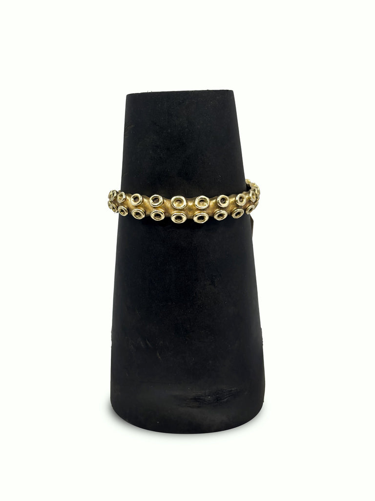 Gold bracelet on a black velvet stand against a white background